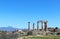 The ruins of the Temple of Apollo at ancient Corith Greece with a church and village and high mountains in the background