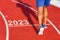 Runner crosses the line starting in 2023 on a red treadmill with the numbers 2023. New year entry concept, step