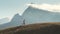 A runner strenuously runs along the top of the holna against the backdrop of a picturesque mountain. The person moves