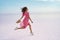 Running carefree woman on salt flats on pink lake. Brunette model in pink adorable flowing dress