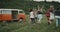 Running group of stylish friends in the middle of field, behind a retro orange van.