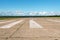 The runway of a rural small airfield against a blue sky with clouds of the airfield. Lonely airfield.