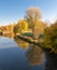 Rural autumnal river scene with blue sky, colorful trees reflecting on the water