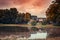 Rural buildings by a reflective pond with fallen autumn foliage on the water surface in Burgerpark