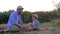 Rural child with bandage on his injured knee is sitting next to his dad in straw hats and shows thumbs up