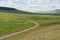 The rural dirt road goes beyond the horizon along the green steppe.