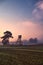 Rural foggy landscape with silhouette of a hunting tower on a field at sunrise