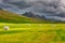 Rural icelandic summer daytime landscape with packaged mown hay, green field, farm, mountains and dramatic cloudy sky, Iceland