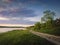 Rural landscape with a country road between lake and forest. Idyllic summer scene, peaceful evening with colorful sunset sky