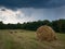 Rural landscape with hay stacks, field with roll bales near forest, domestic livestock fodder during wintertime, summer shower
