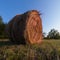 Rural landscape with one roll bale in field during dusk, straw haystack as cattle fodder