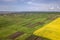 Rural landscape on spring or summer day. Aerial view of green, plowed and blooming fields, house roofs on sunny dawn. Drone