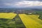 Rural landscape on spring or summer day. Aerial view of green, plowed and blooming fields, house roofs on sunny dawn. Drone