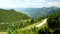 Rural landscape surrounded by overgrown alps mountains with trees during summer day