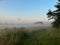 Rural landscape. A wooden log house surrounded by meadows and bushes shrouded in mist