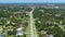 Rural road with driving traffic cars in American small town in Florida. Private homes between green trees and suburban