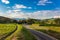 Rural Road Among Grean Fields. Amazing Blue Sky With Beautiful Clouds, Mountains, Meadow With Fresh Green Grass. Highway In Rio.