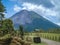 Rural road with green vegetation against the background of Arenal Volcano. Costa Rica.