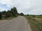 Rural road with  trees on the right beautiful overcast sky over a field and a rural road