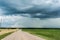 Rural sandy road runs through a field sown with wheat. Large gloomy clouds of a storm cyclone. Rainy season