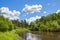 Rural summer landscape with forest, river, blue sky and white cl