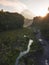 Rural view of river and lava path surrounded by dense of forest with mountain background and blue sky in sunrise time