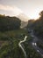 Rural view of river and lava path surrounded by dense of forest with mountain background and blue sky in sunrise time