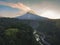 Rural view of river and lava path surrounded by dense of forest with mountain background and blue sky in sunrise time