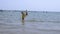 RUSSIA, IZBERBASH - 12 JULE, 2021: A little boy in a yellow life jacket with a fishing rod walks on the sea, laughs and