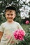 Russia, June 2020 - portrait of a cute touching little four year old kid boy with a pink peony flower in full bloom in the village