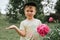 Russia, June 2020 - portrait of a cute touching little four year old kid boy with a pink peony flower in full bloom in the village