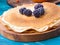 Russian pancakes on a wooden plate on an azure table with frozen blackberries. Closeup