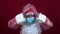 Russian santa claus in a medical mask on a red background, upset, holds his head with two hands