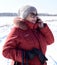Russian senior woman talking on phone against snowy field. winter