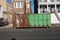 A rusted green dumpster on an asphalt street in front of two buildings