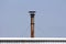 Rusted metal industrial chimney held together with two strong wires on roof of building at abandoned industrial complex