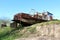 Rusted metal river barge left unused on edge of river bank surrounded with grass and dry soil on clear blue sky background