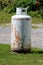 Rusted old light grey propane tank or grill cylinder used for powering barbeque grill left outside of family house