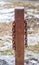 Rusted square metal post with two hanging chains.