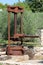 Rusted strong metal vintage olive oil press machine mounted on concrete foundation used as garden decoration with stone wall and