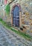 Rustic arched wooden door on stone wall and stone paved alley with shapes