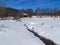 Rustic Barn Across Snowy Field with Creek and Mountains