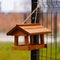 Rustic birdhouse hanging from the back of a weathered wire fence in a rural outdoor setting