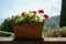 Rustic ceramic flowerpot with red geranium flowers on a garden wall in front of a sunny landscape