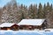 Rustic farmhouse and barn in snowy winter landscape at fir forest