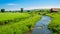 A rustic farmhouse, green fields, and a winding river under a clear blue sky