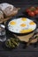 Rustic fried eggs on a dark wooden table with tomatoes, a glass of vodka, beacon, bread and pickled gherkins. in a dark key