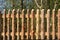 A rustic garden fence made of small logs with bark on it stands on the edge of a garden with trees in the background