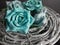Rustic gray wood coiled up like a nest with teal blue paper rose flower blooms piled on it in a close macro shot