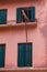 Rustic Iron Steel Supporting a Wood Plank Hanging Horizontally from High Windowsill. Old Apartment Building with Pink